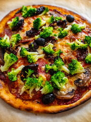 Pizza with broccoli and black olives on baking paper