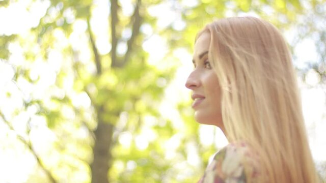 Video clip, blur effect and light fler, a young blonde woman with long hair in a long dress walks in a blossoming apple orchard on a sunny day in spring.