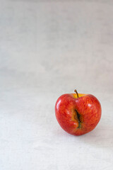 Red organic ugly apple on grey cement background with copy space. Fruit with unusual shape. Buying imperfect product to reduce food waste. Sustainable consumption. Vertical. Fresh food, eco trend.