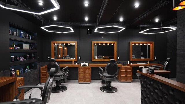 Vintage barbershop interior - movement along the chairs, wooden tables and  mirrors. Stylish hair studio indoors. Stylish beauty salon design with  modern lighting and lamps.