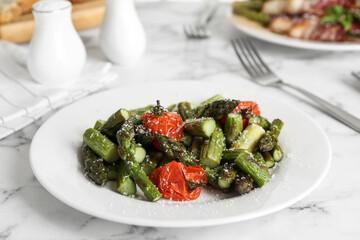 Oven baked asparagus with cherry tomatoes on white plate