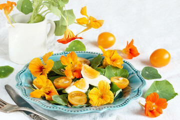 salad with nasturtium leaves and flowers of the plant. bright summer salad with edible  flowers and yellow tomatoes with egg, sunflower seeds.