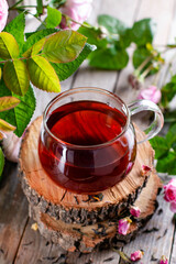 Tea in a glass cup with rose petals and fresh flowers on a wooden table