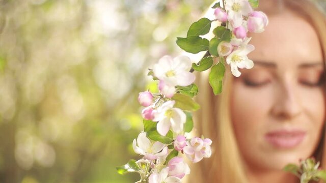 Video clip, blur effect and light fler, a young blonde woman with long hair in a long dress walks in a blossoming apple orchard on a sunny day in spring.