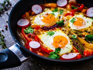 Shakshuka - fried eggs with vegetables in frying pan
