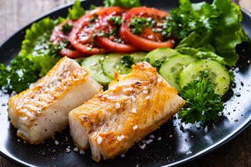 Fish dish - fried cod fillet with vegetables on wooden table
