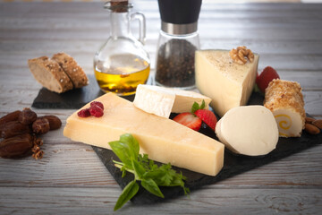 Cheese plate served with dried fruits, strawberry and olive oil, on a black board