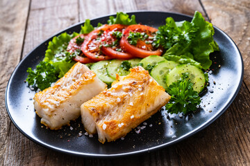 Fish dish - fried cod fillet with vegetables on wooden table
