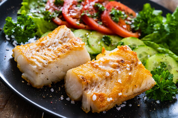 Fish dish - fried cod fillet with vegetables on wooden table
