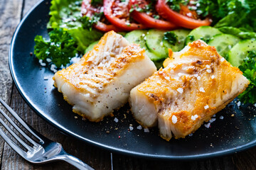 Fish dish - fried cod fillet with vegetables on wooden table
