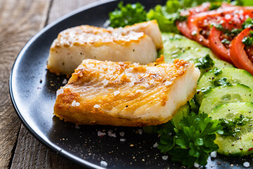 Fish dish - fried cod fillet with vegetables on wooden table
