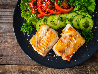 Fish dish - fried cod fillet with vegetables on wooden table