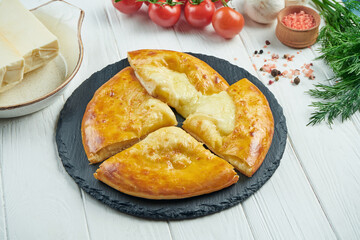 Close up view on tasty traditional Khachapuri - closed baked pie stuffed with melted salt cheese (suluguni) or meat on black tray. Traditional georgian food