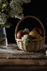 fresh red apples and blossom branches in basket on dark wooden background