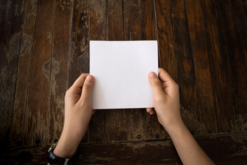 Woman hand holding white paper with wooden table background.