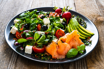Breakfast - smoked salmon, feta cheese, avocado and vegetable salad on wooden table
