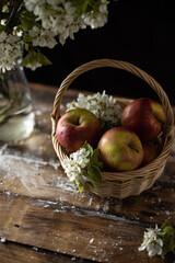 fresh red apples and blossom branches in basket on dark wooden background