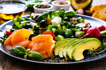Breakfast - smoked salmon, feta cheese, avocado and vegetable salad on wooden table
