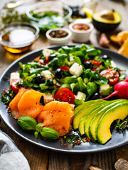 Breakfast - smoked salmon, feta cheese, avocado and vegetable salad on wooden table
