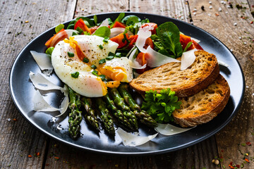 Boiled egg with bread, asparagus, parmesan and vegetable salad on wooden table