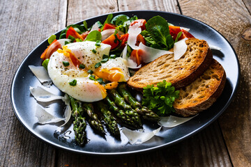 Boiled egg with bread, asparagus, parmesan and vegetable salad on wooden table