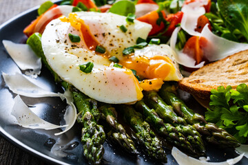Boiled egg with bread, asparagus, parmesan and vegetable salad on wooden table