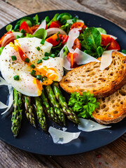 Boiled egg with bread, asparagus, parmesan and vegetable salad on wooden table