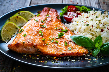 Fried salmon steak with rice and vegetables on wooden table
