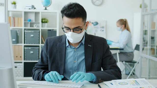 Slow motion of Arab man working with computer in office taking off face mask feeling discomfort during corona virus quarantine. People and business concept.