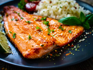 Fried salmon steak with rice and vegetables on wooden table
