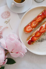 A cup of coffee, berry tartlet with fresh berries and peonies. Flat lay, composition. Coffee, dessert and flowers. Concept of coffee shop, cafe and flower shop.