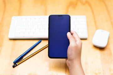 Girl hand holding smart phone with Black blank empty screen on desk table.