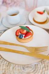 Fototapeta premium A cup of coffee, berry tartlet with fresh berries and peonies. Flat lay, composition. Coffee, dessert and flowers. Concept of coffee shop, cafe and flower shop.