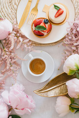 A cup of coffee, berry tartlet with fresh berries and peonies. Flat lay, composition. Coffee, dessert and flowers. Concept of coffee shop, cafe and flower shop.