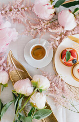 A cup of coffee, berry tartlet with fresh berries and peonies. Flat lay, composition. Coffee, dessert and flowers. Concept of coffee shop, cafe and flower shop.