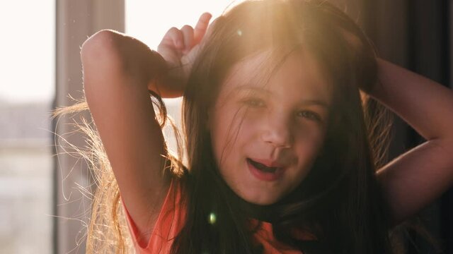 Portrait of a brunette girl against the setting sun. Beautiful baby looking at the camera, laughing and making faces