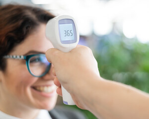 Mandatory measurement of a fever non-contact thermometer gun of all office workers. Happy woman with normal body temperature. Infrared portable device needed during an epidemic.