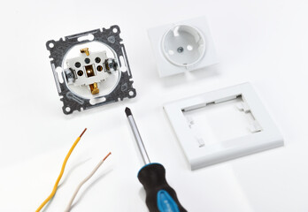 The cost of electrical work and repair. A disassembled socket is next to a screwdriver on a white background.