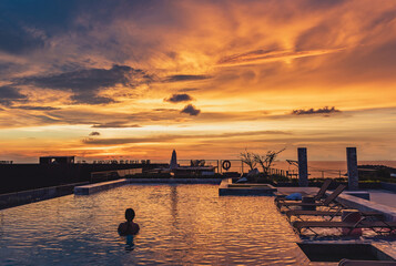 Fototapeta premium Silhouette of asian woman standing in the pool and looking to sunset view with chilling location on golden hour time.