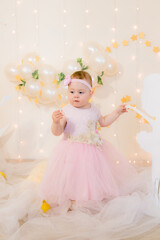 Cute little girl in a pink princess dress with a flower on her hair plays with wooden ballerinas among the golden stars on the background of a large white wooden moon and balloons. Children's decor. 
