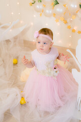 Cute little girl in a pink princess dress with a flower on her hair plays with wooden ballerinas among the golden stars on the background of a large white wooden moon and balloons. Children's decor. 

