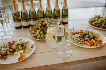 Plates with white grapes, a jug of lemonade, many bottles of champagne, two glasses of champagne. Banquet, catering.