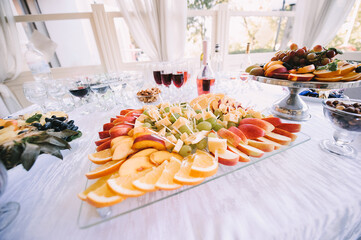 Fruits on a plate, Sliced apples, oranges, peaches, grapes and cheese. Reception, catering. The table is covered with a white tablecloth. 