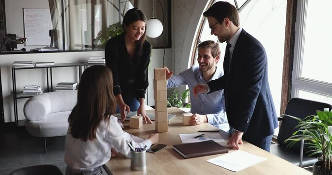 Happy successful multicultural business team people building tower of wooden bricks on office desk. Group teamwork effective strategy, professional partnership organization, help and synergy concept.