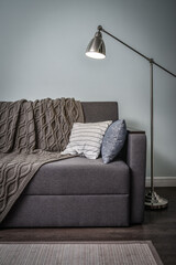 Grey couch with cushions, knitted plaid  and  floor lamp
