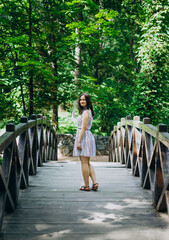 Sofia Park, Uman. Smiling girl in a summer board on a wooden bridge. The girl stands on the bridge among the green summer park. Walk in the summer green forest.