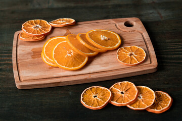 Heap of slices of fresh and dry oranges on rectangular wooden chopping board
