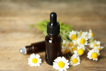 Bottles of essential oil and chamomiles on wooden table