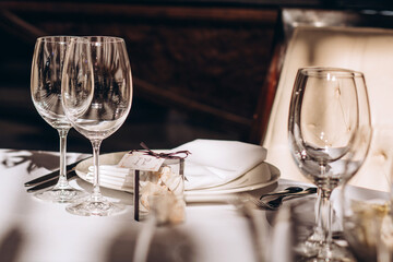 Table setting for a wedding party. a round table with a white tablecloth, glasses, white plates in the rays of the setting sun.