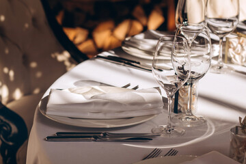 Table setting for a wedding party. a round table with a white tablecloth, glasses, white plates in the rays of the setting sun.